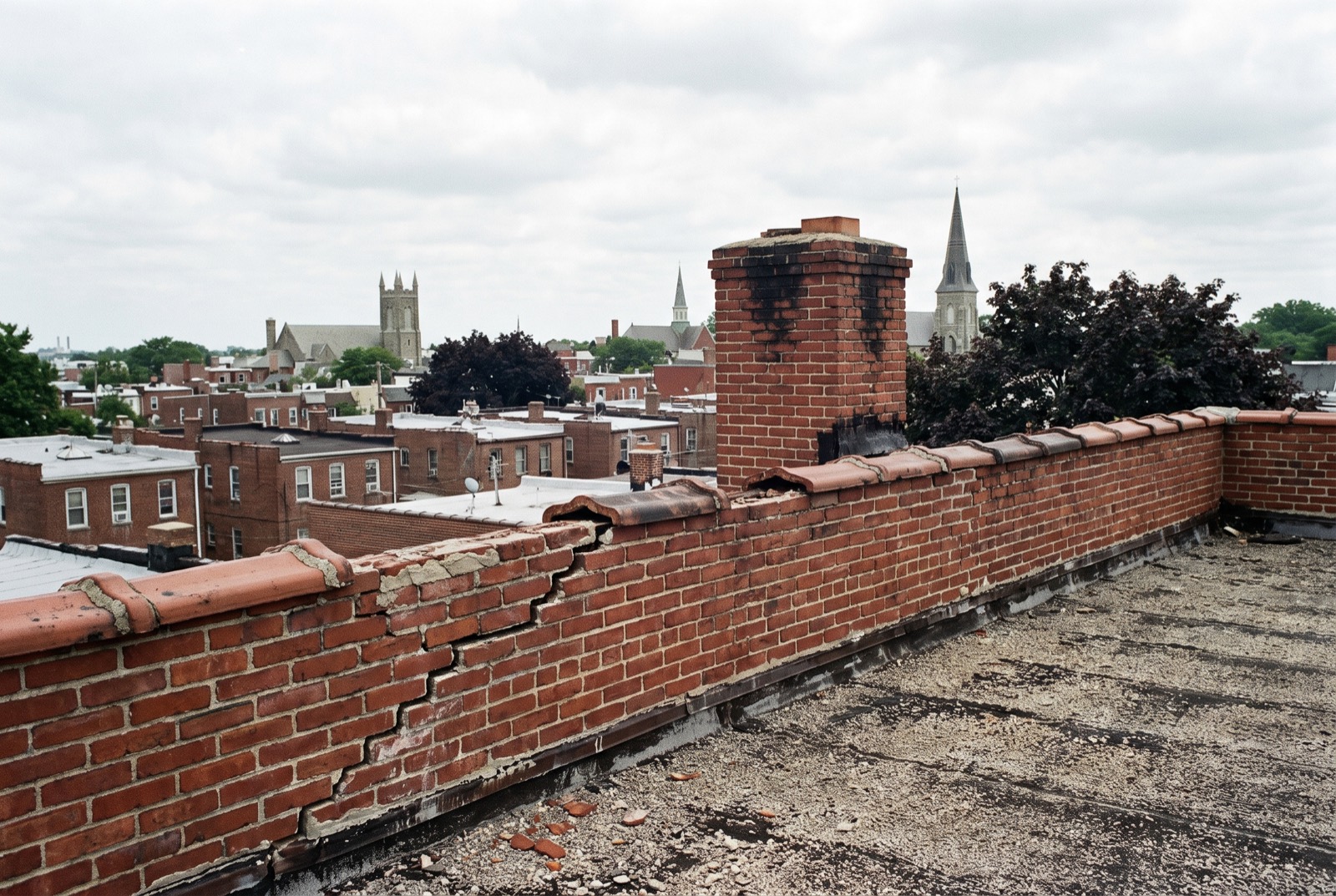 A brick parapet with a stepped crack and broken clay coping, a chimney behind it